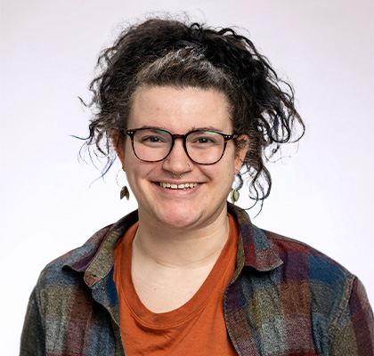 Headshot of Lee Spindler, a woman with long black hair, black glasses and wearing an orange shirt with a colorful flannel button down shirt