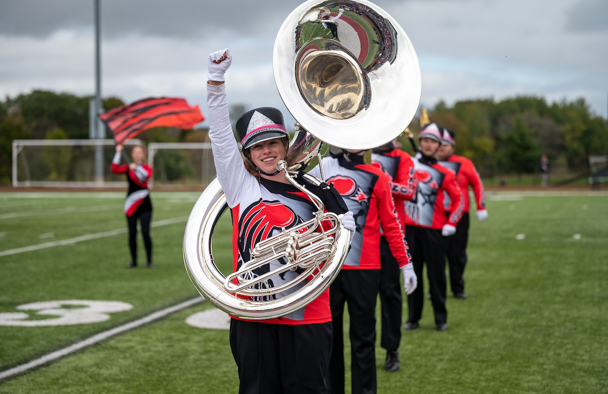 a marching band member holds a tuba and one arm in the air