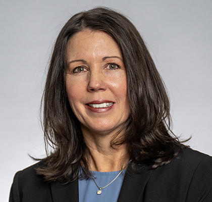 Michelle Benedict headshot. A white woman with shoulder length dark hair is wearing a blue top, necklace and black blazer.