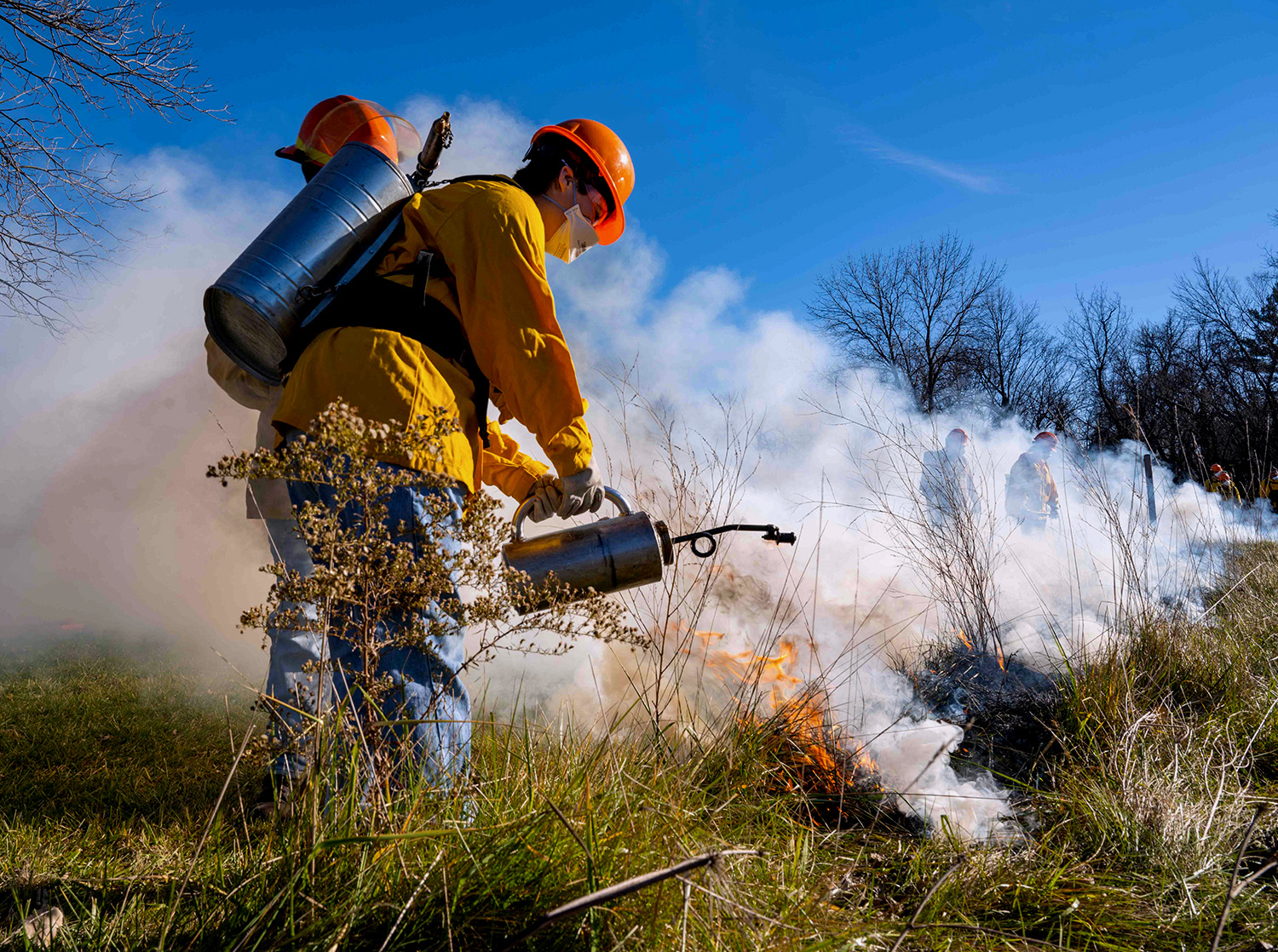 A student wears fire protective gear and assists with a planned prairie burn as part of the Ecological Restoration Institute