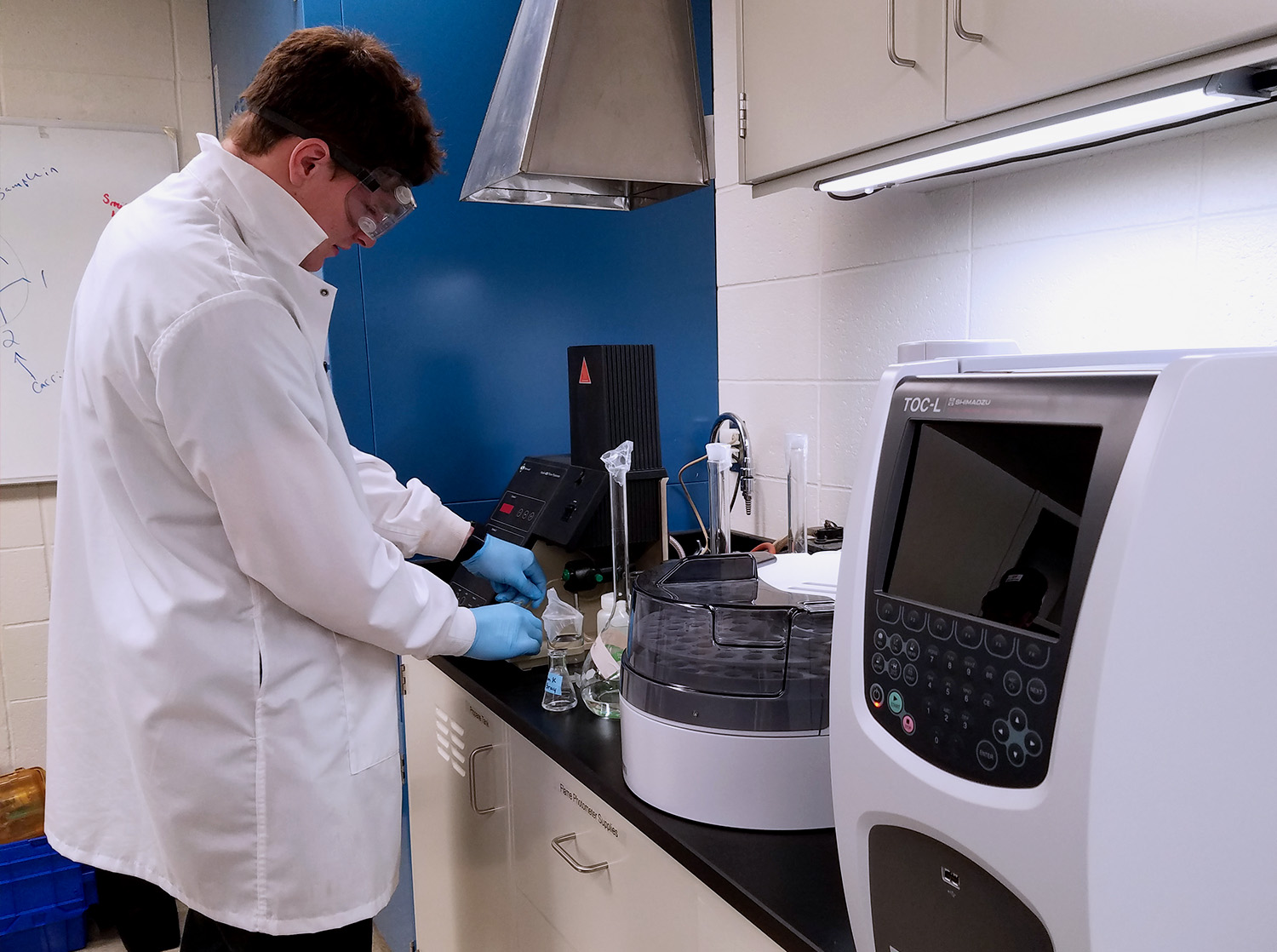 A male student stands in front of lab equipment conducting research