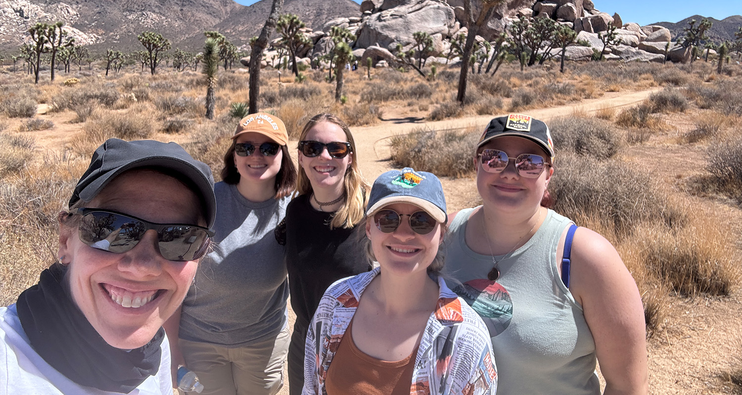 A group of 5 people take a selfie on an academic field trip in a desert