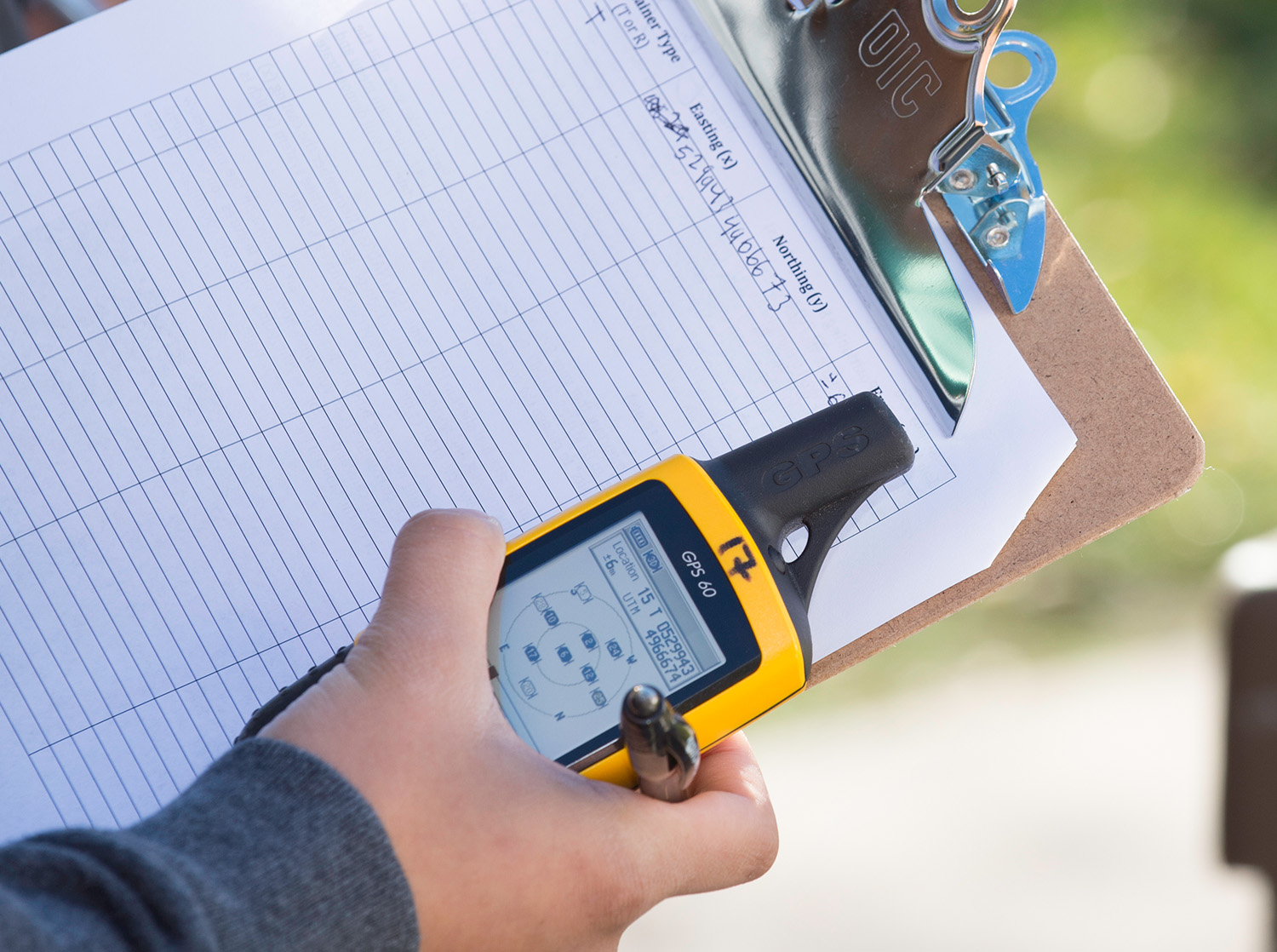 A student holds a mapping device and a clipboard during a class exercise outside