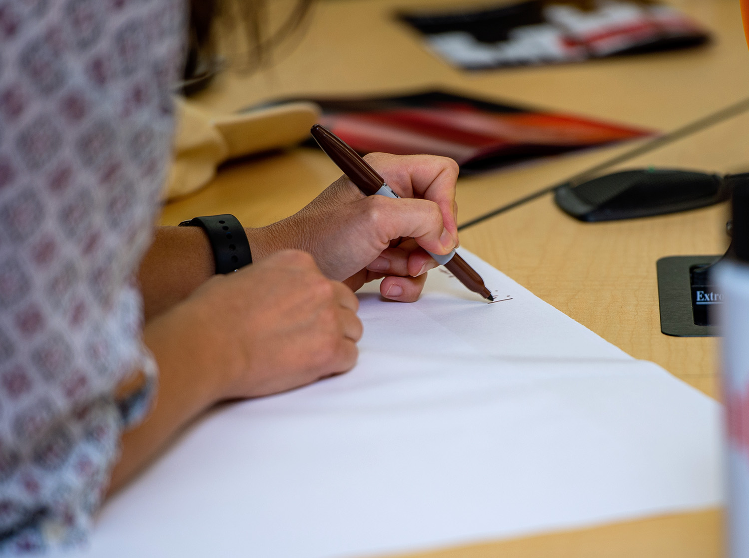 A student writes on a piece of paper with a brown Sharpie