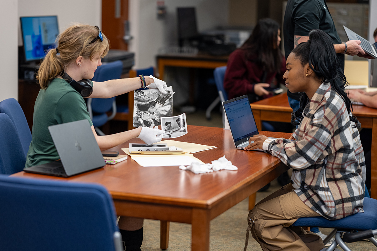 Two women sit at a table looking at historical photos
