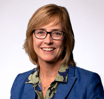 Headshot of Sonja Maki, a woman with short blonde hair and glasses wearing a green blouse and blue blazer