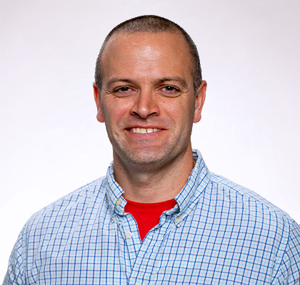 Headshot of Timothy Mills, a man with short black hair and a blue plaid button down shirt