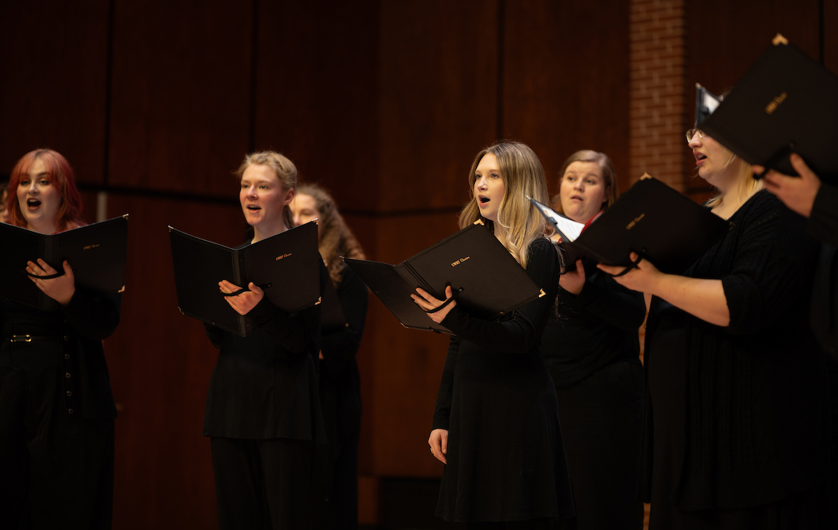 choir singers wearing all black hold song books and perform on a stage
