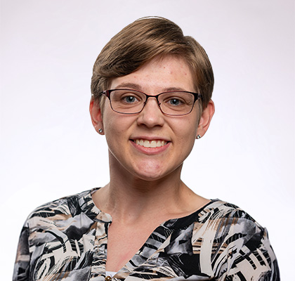 Headshot of Zoe Foster, a woman with short brown hair and brown glasses wearing a black and white patterned blouse