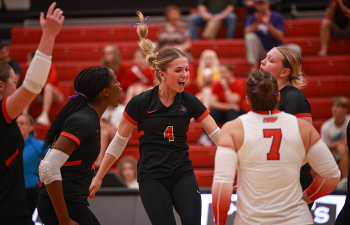 a volleyball player wearing a black uniform celebrates with teammates on the court