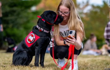 A female student prepares to take a picture with a black lab for a companion animal course