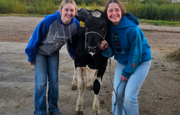 Two students pose with a calf outside of Mann Valley Farm