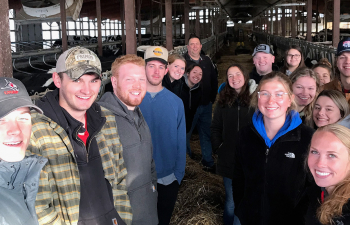 A group of agricultural business students stand in a barn at Mann Valley Farm