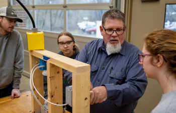 A professor helps two students construct a box out of wood during a lab demonstration