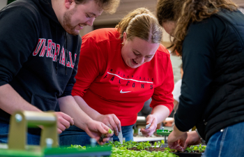 A female and male student practice transplanting seedlings into plastic trays