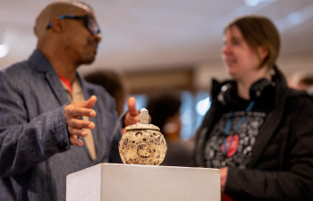 Two people discuss an art piece on a pedestal in the student gallery of KFA.