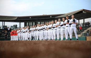 a baseball team in all white uniforms stands for the national anthem on a baseball field