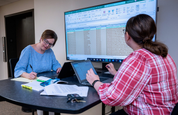 Two people look at an excel spreadsheet projected on a large TV