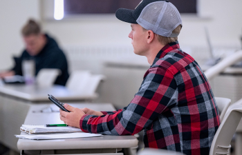 A male student holds a calculator and listens to the professor
