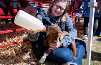 A female student feeds a baby goat using a bottle