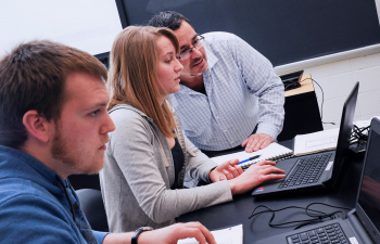 Professor Fred Bonilla assists two students during an exercise in the classroom