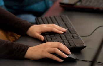 A student's hands rest on a computer keyboard and mouse