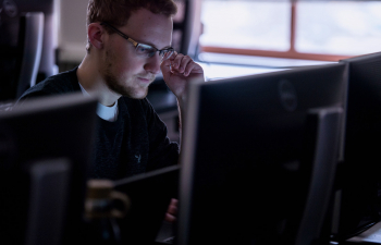 A male students face is lit up by the glow of a computer screen