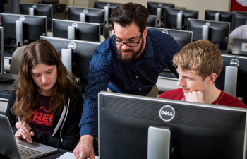 A faculty member points to text in a textbook while working with two students