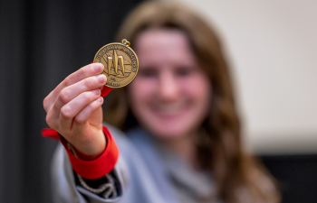 A female student holds a medal out to the camera