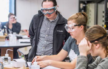 Professor Samuel Alvarado stands over two students working on a lab exercise