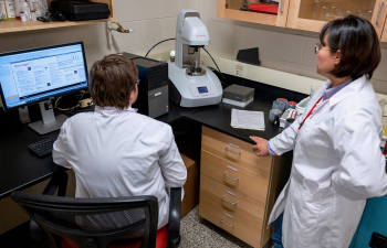 A professor and student stand and observe a large tube during an experiment