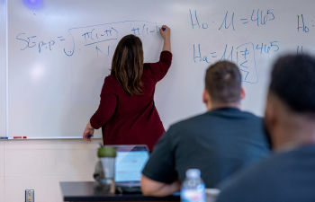 A female professor writes an equation on a whiteboard