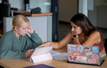 A female tutor helps another female student understand their class homework