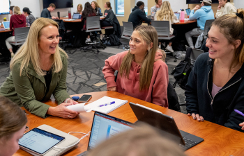 A female professor speaks with two female students at a table during class