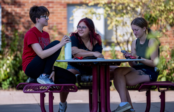 Three students sit on a table enjoying the weather outside