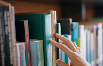 A student skims their hand over books on shelves in the library