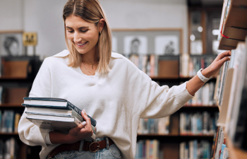 A female student holds library books and browses the shelves
