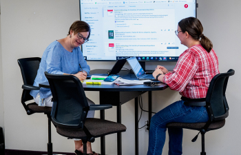 Two people sit in front of a computer monitor to work on a project