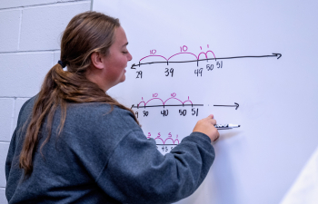 A female student writes a math problem on a whiteboard