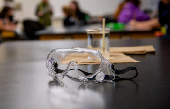 A pair of safety goggles sit on a lab table in a physics lab