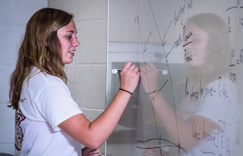 A female student works on a math equation on a whiteboard