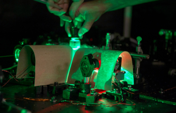 A person adjusts the dials on a green laser in a physics classroom