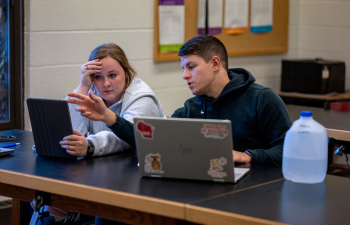 Two students sit at a desk working together during class