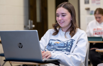 A female student sits at a desk using their laptop