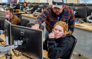 A tutor points to something on a computer screen while another student looks on