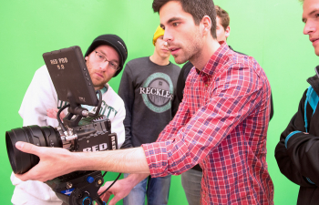 A group of students configure a video camera in front of a green screen