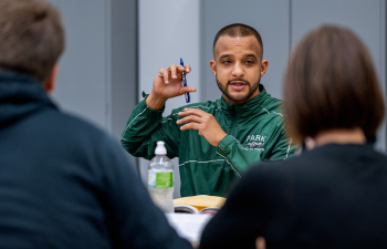 A male student gestures to others sitting at the same table explaining a topic