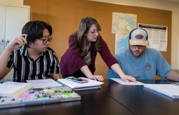 A female professor helps two male students with their coursework during class.
