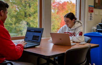 Two students sit at a table working on a project together