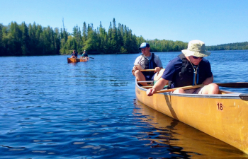 Two male students sit in a canoe and two other students are behind them in the background